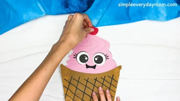 hand gluing the cherry of paper plate ice cream craft template