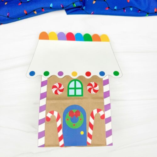 Finished gingerbread house paper bag craft decorated with candy canes, peppermint swirls, and colorful rooftop lights, a cheerful Christmas project for kids.
