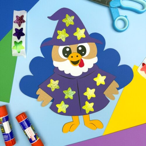 Finished wizard turkey disguise craft featuring a purple robe and hat decorated with glitter star stickers, surrounded by glue sticks, scissors, and colorful paper—an imaginative and easy Thanksgiving project for kids.