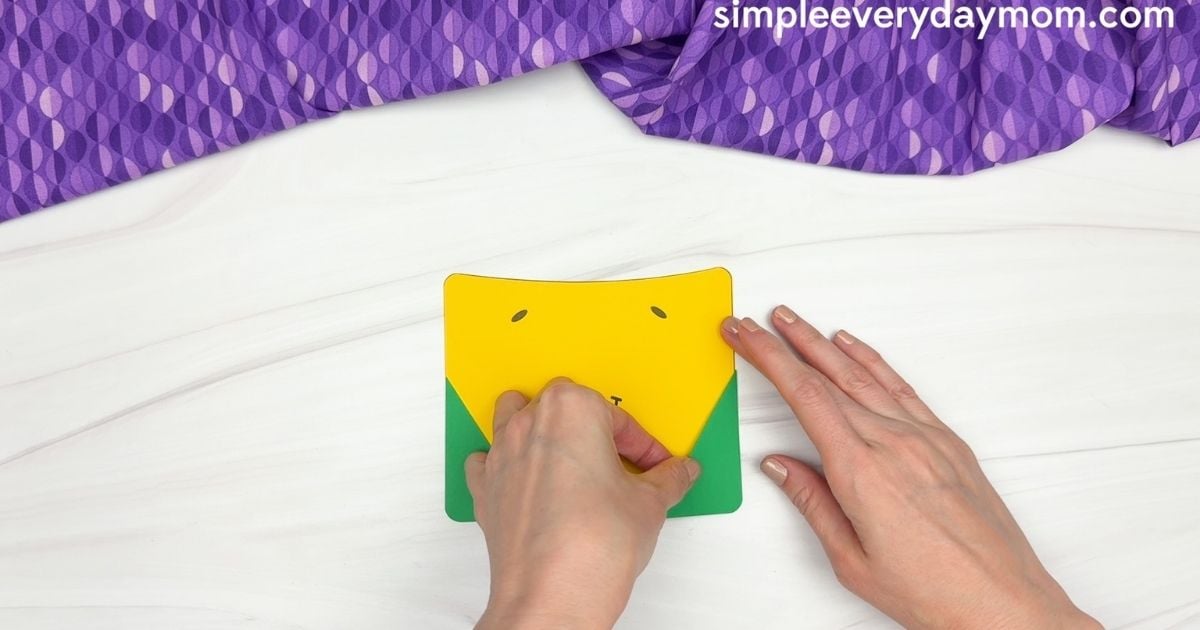 Hands assembling the yellow and green base of the crayon box craft.