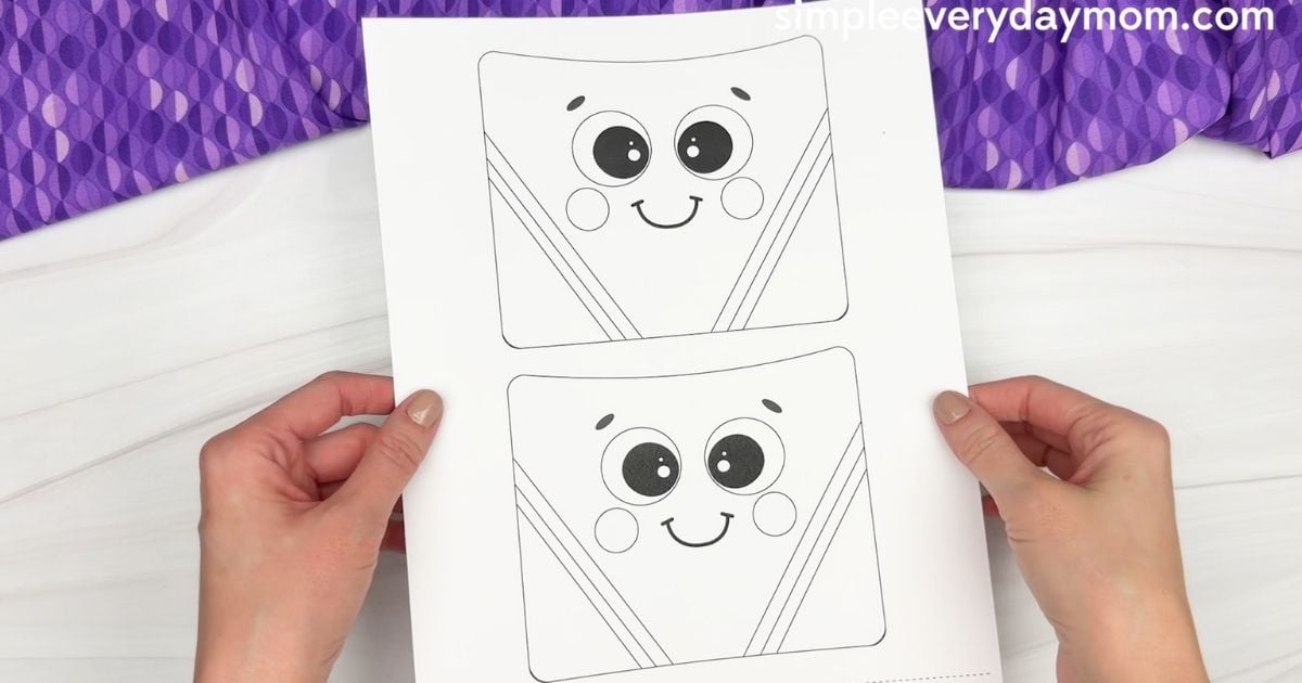 Hands holding a printable crayon box template sheet with two outlined smiling faces.