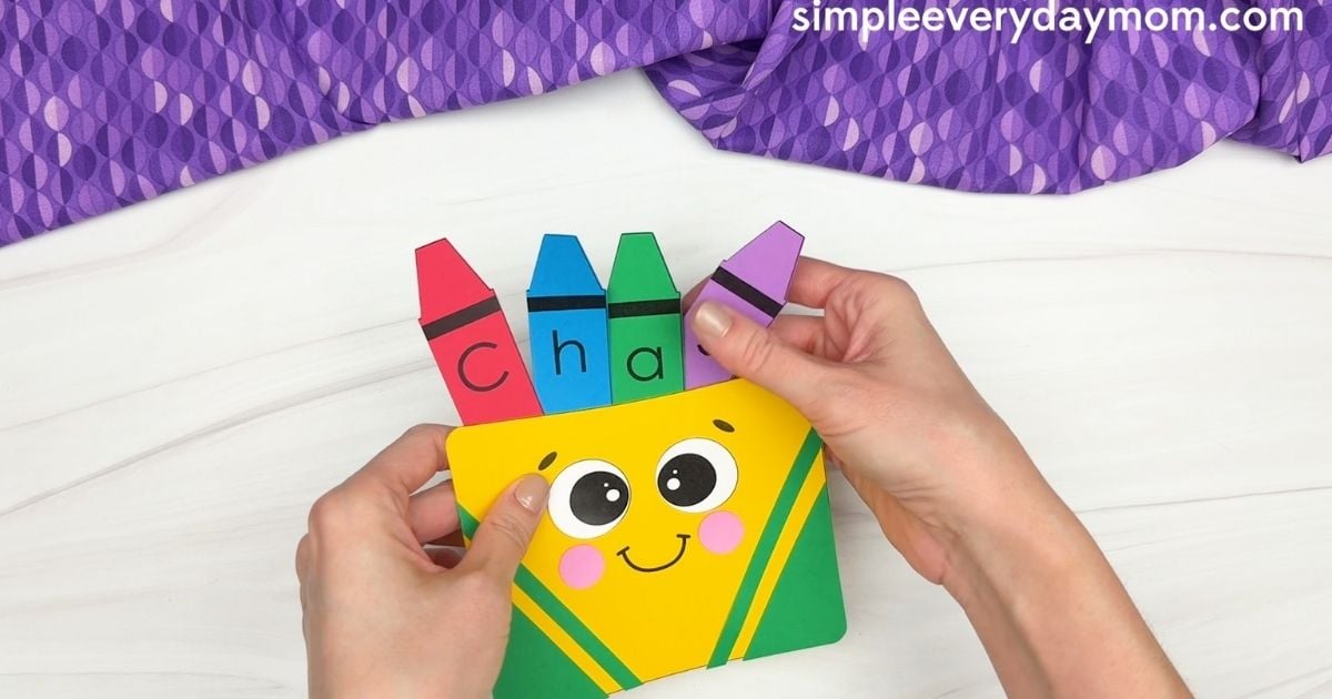 Hands inserting lettered paper crayons into the box to spell “Chase.”