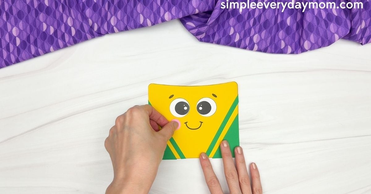 Hand attaching a pink cheek to the crayon box craft.