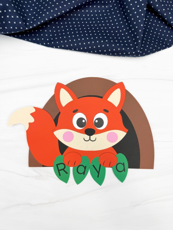 Completed fox name craft featuring a smiling paper fox with pink cheeks and green leaf cutouts spelling “Raya.” This fun woodland animal activity is perfect for preschool and kindergarten kids learning name recognition and practicing fine motor skills.