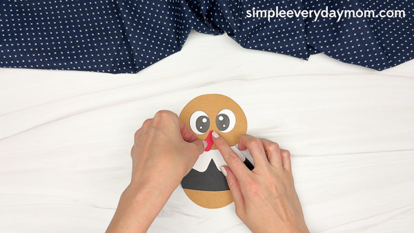 Hands placing a red snood onto the paper pilgrim's face.