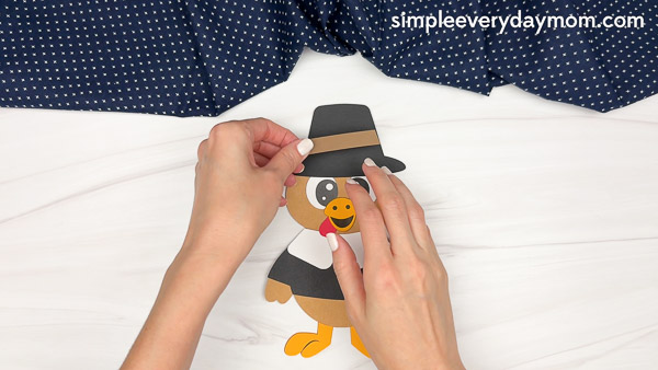 Hands placing a brown paper strip as a band and yellow paper buckle on the black pilgrim hat.