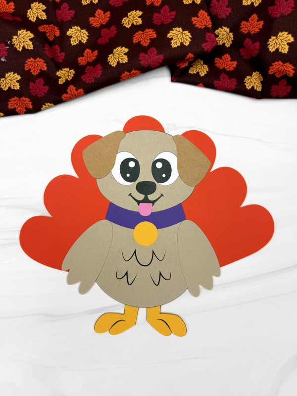 Adorable paper dog dressed as a turkey, featuring a brown body, red heart-shaped feathers, and a purple collar, a cute Thanksgiving kids activity.