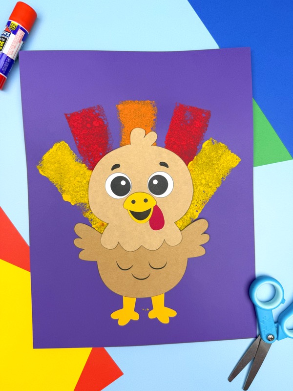 Colorful sponge painted turkey on a purple paper background with red, yellow, and orange textured feathers, ready for a Thanksgiving display.