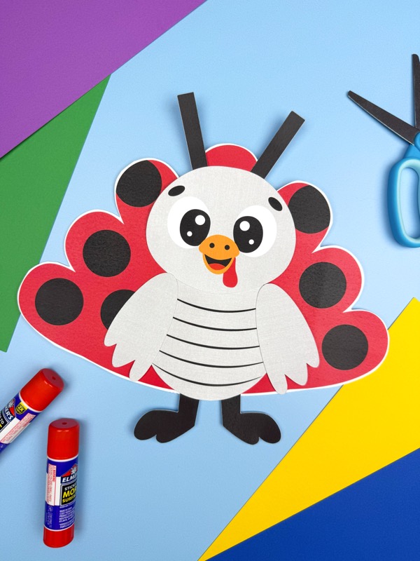 A completed craft, this festive paper turkey ladybug is displayed on a blue background with colorful paper shapes, scissors, and glue sticks.