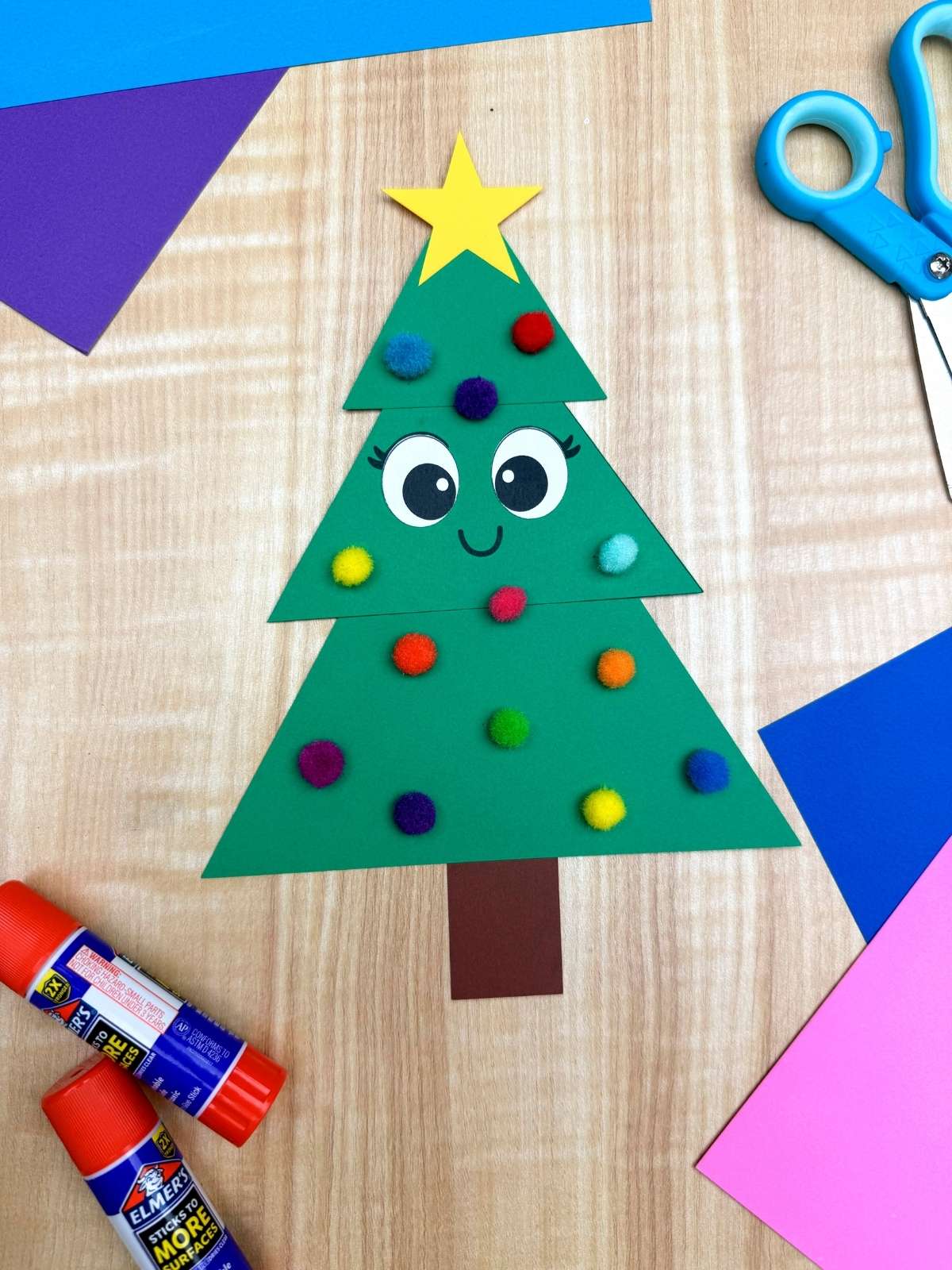 A completed Craft of a paper Christmas tree surrounded by craft supplies on a wood background.
