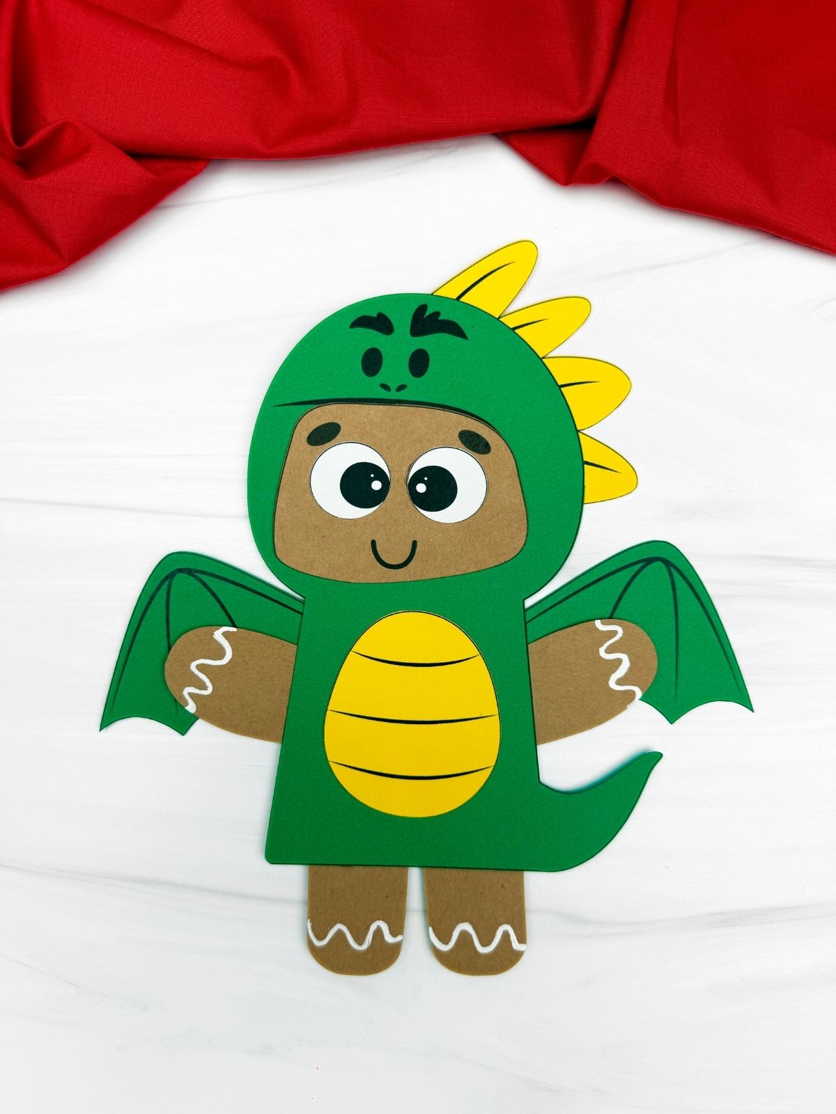 A completed craft showing a paper gingerbread man dressed in a green dragon disguise with yellow accents.