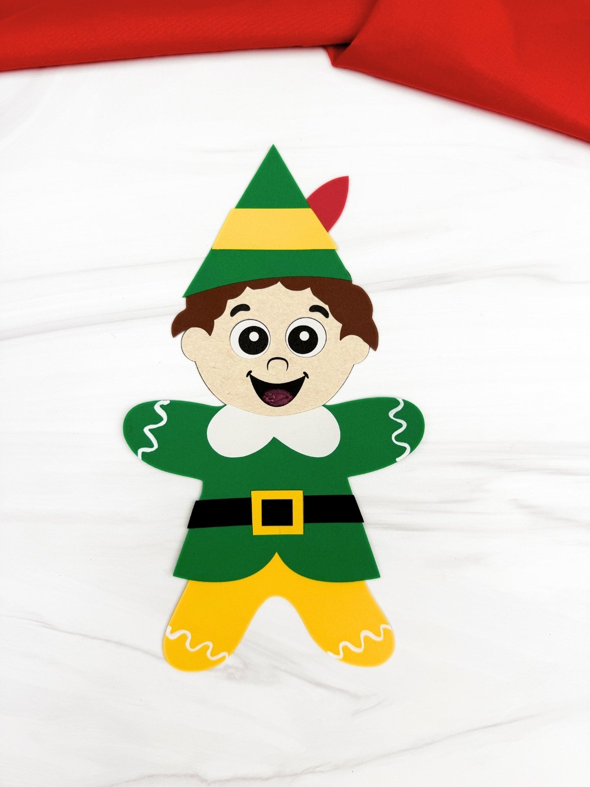 A completed Craft featuring a Buddy the Elf gingerbread man paper disguise with green outfit yellow pants elf hat and icing details for an easy printable Christmas craft for kids.