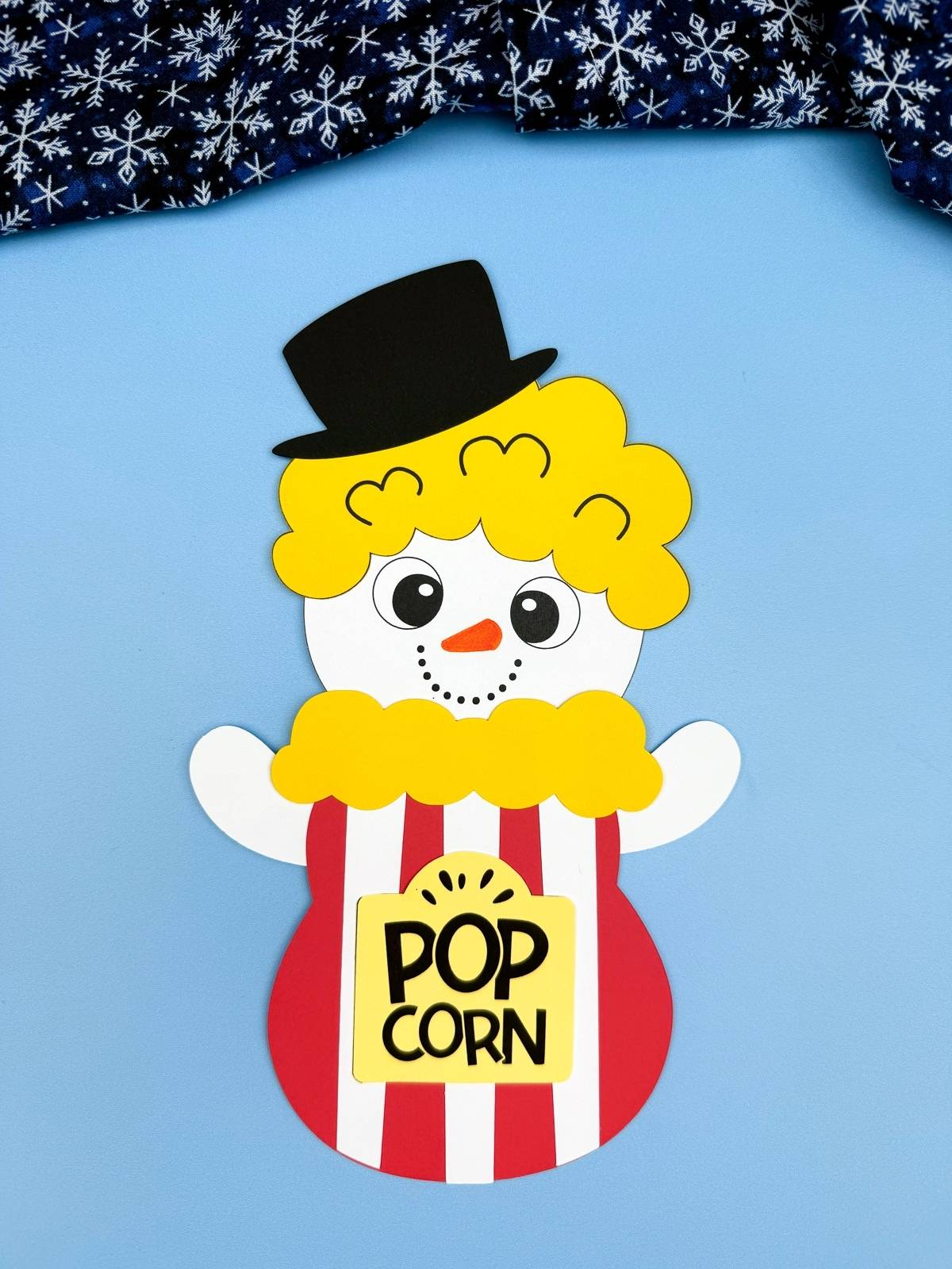 A completed Craft showing a popcorn snowman disguise made from paper with a smiling snowman inside a red and white popcorn box, a fun winter craft for kids using a printable template.