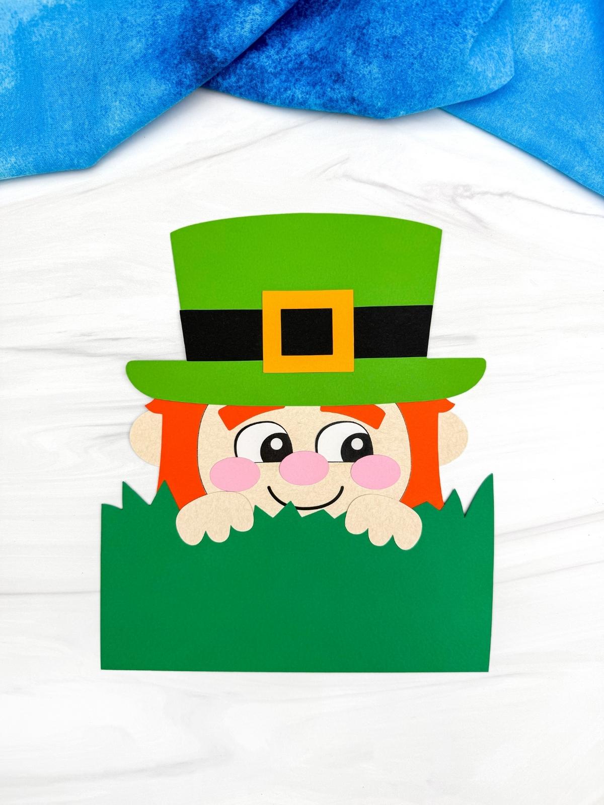 A completed craft of a Sneaky Leprechaun paper craft with green hat and grass for a St. Patrick’s Day kids activity.