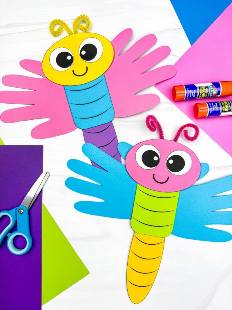 A completed craft showing two colorful dragonfly handprint paper crafts with bright wings and smiling faces, a fun and easy spring insect craft for preschool and kindergarten kids.