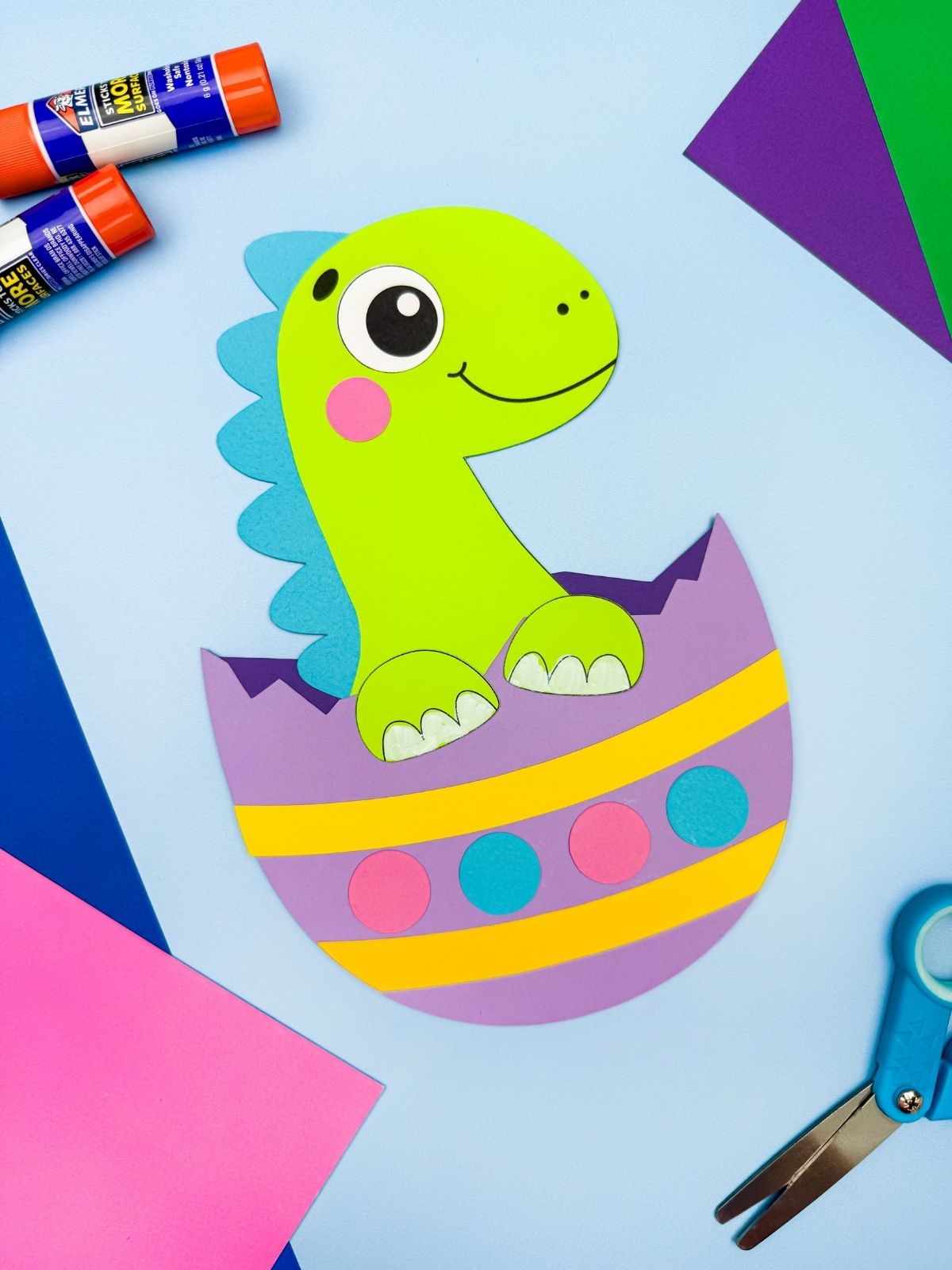 A completed craft of a green dinosaur hatching from a colorful paper Easter egg, easy kids spring dinosaur craft with scissors paper and glue