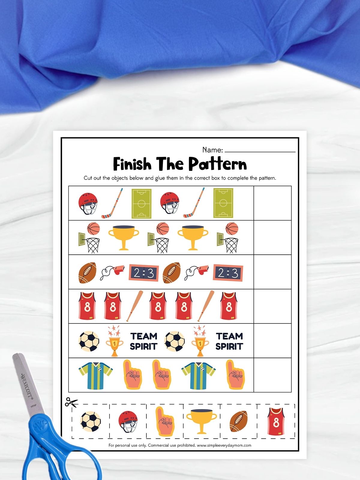 The image shows a children’s worksheet titled “Finish The Pattern” with a sports theme. It features rows of repeating images like helmets, balls, trophies, jerseys, and other sports items, where kids must complete the pattern by cutting and pasting the correct pieces. A pair of scissors is placed beside the page, and the background includes a light surface with blue fabric above.