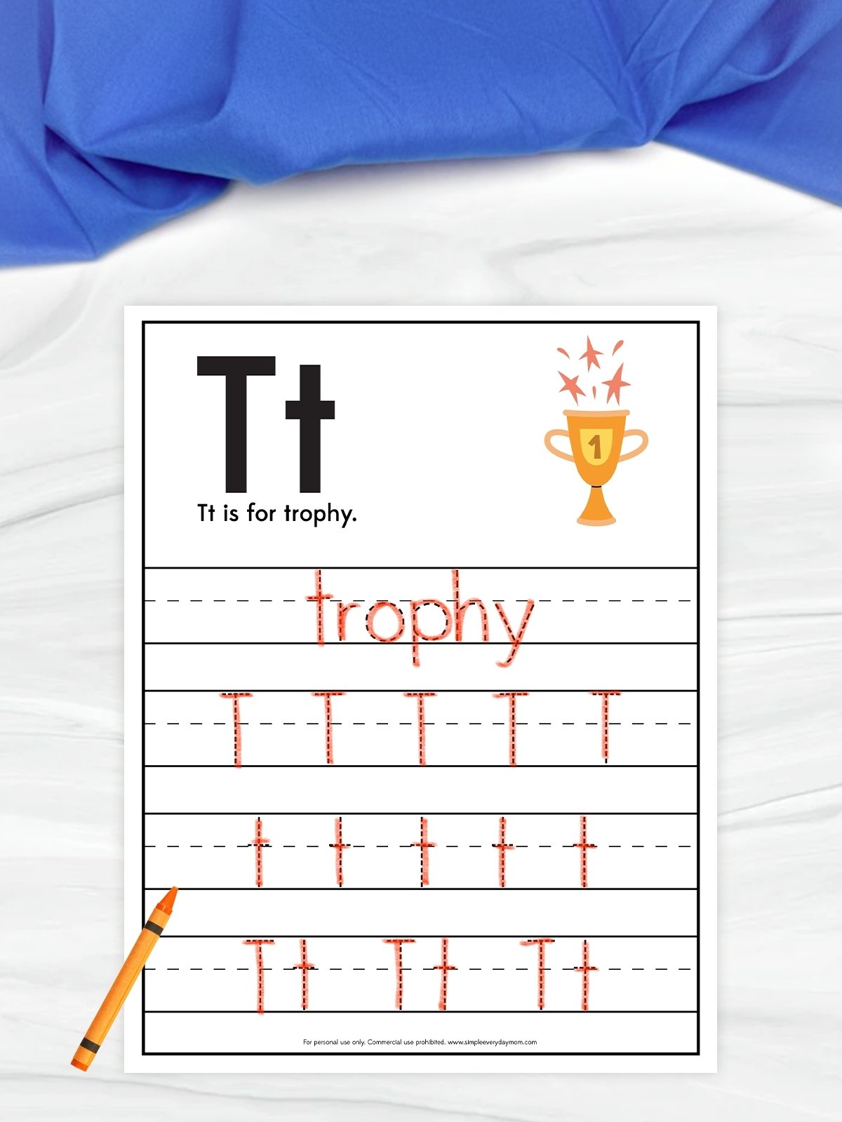 The image shows a children’s letter tracing worksheet focused on the letter “T.” At the top, it includes both uppercase and lowercase T along with a small trophy illustration and the phrase “Tt is for trophy.” Below are dashed lines with the word “trophy” and multiple rows of uppercase and lowercase T’s for tracing practice, with a crayon placed beside the page.