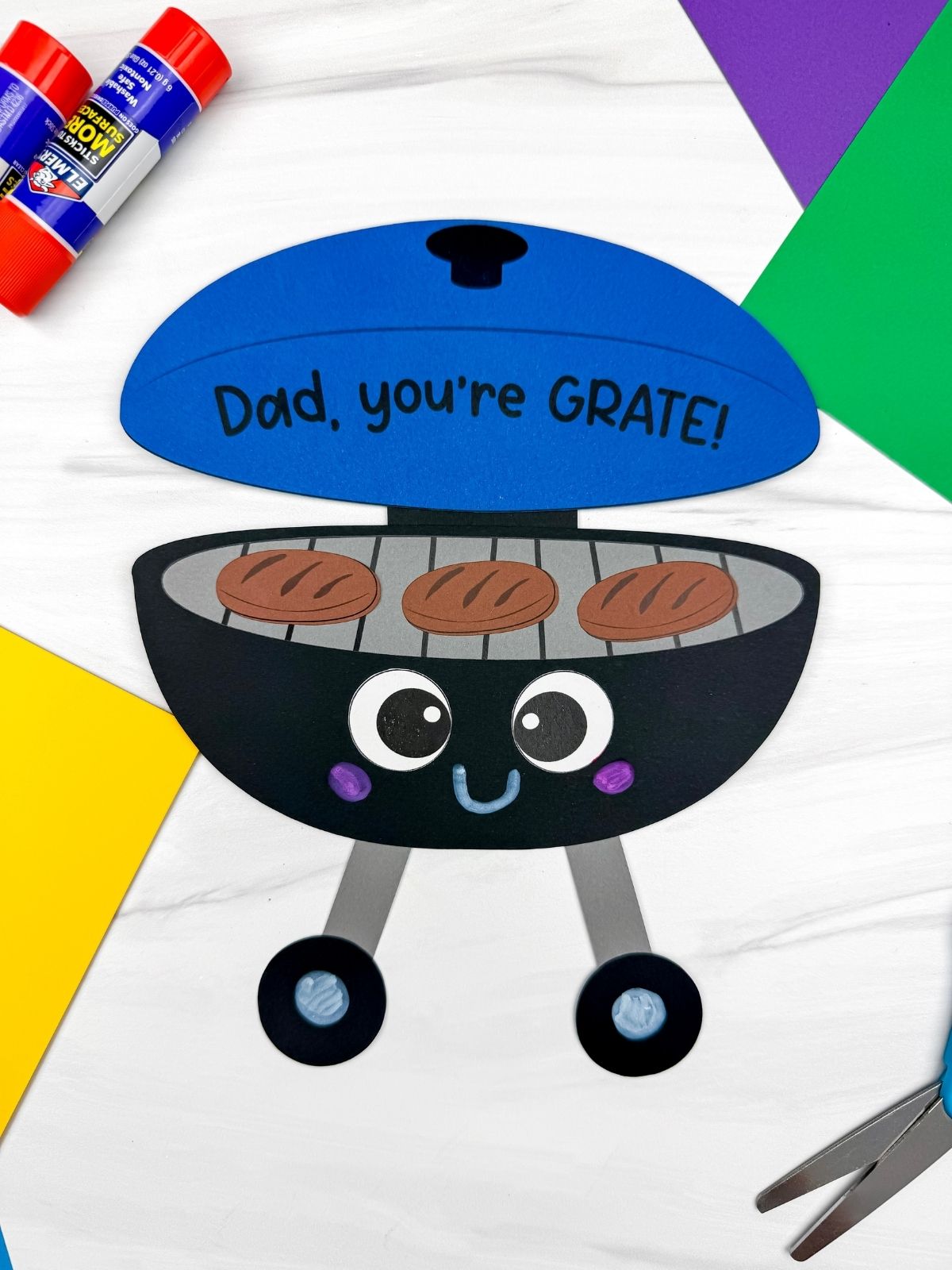 A completed craft showing a Father’s Day grill craft with blue lid and Dad you’re GRATE message surrounded by craft supplies