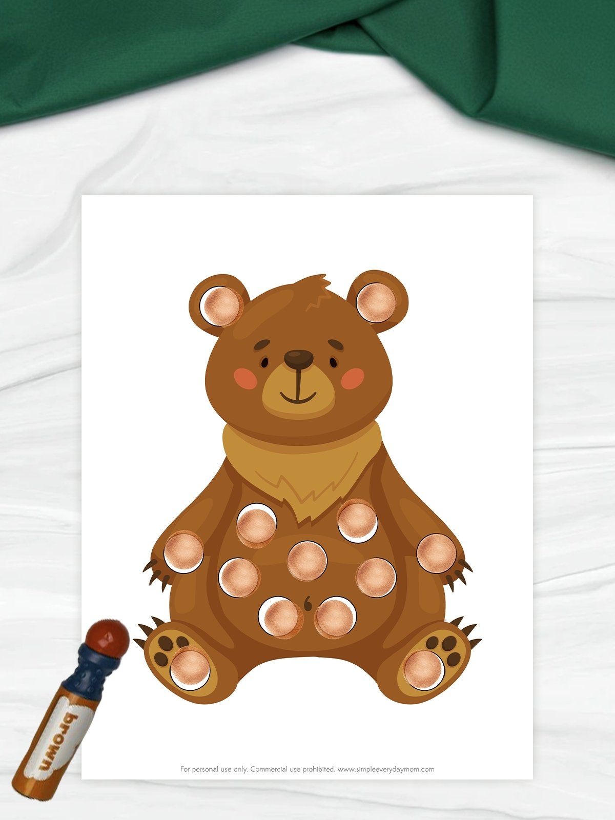 The image shows a cute cartoon bear on a printable worksheet with circles placed across its body. The circles are filled in with a brown dot marker, suggesting a dot marker coloring activity for kids. A brown marker sits beside the page, reinforcing the hands-on, creative nature of the activity.
