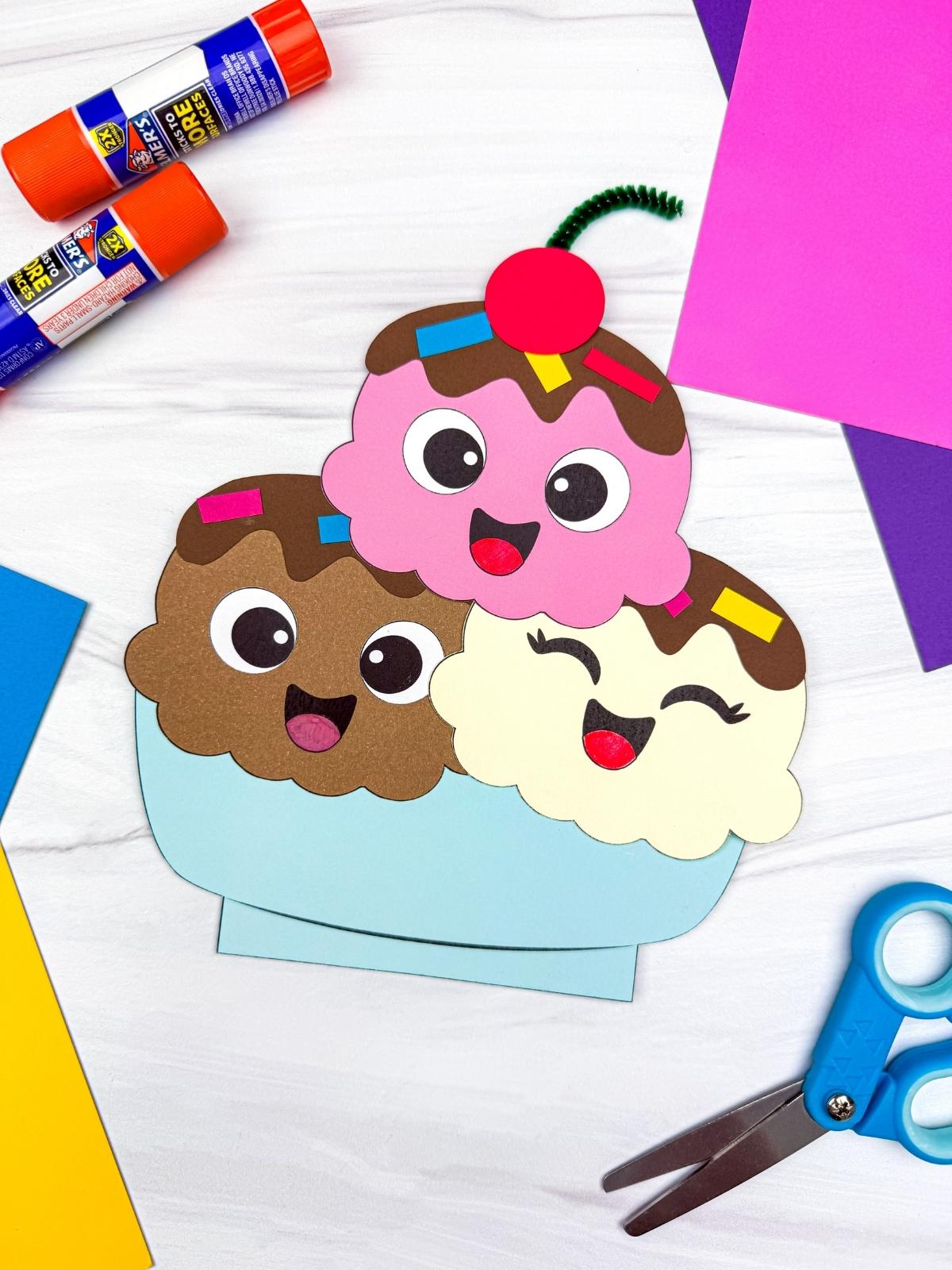 A completed craft of a smiling ice cream sundae with three scoops and craft supplies around it