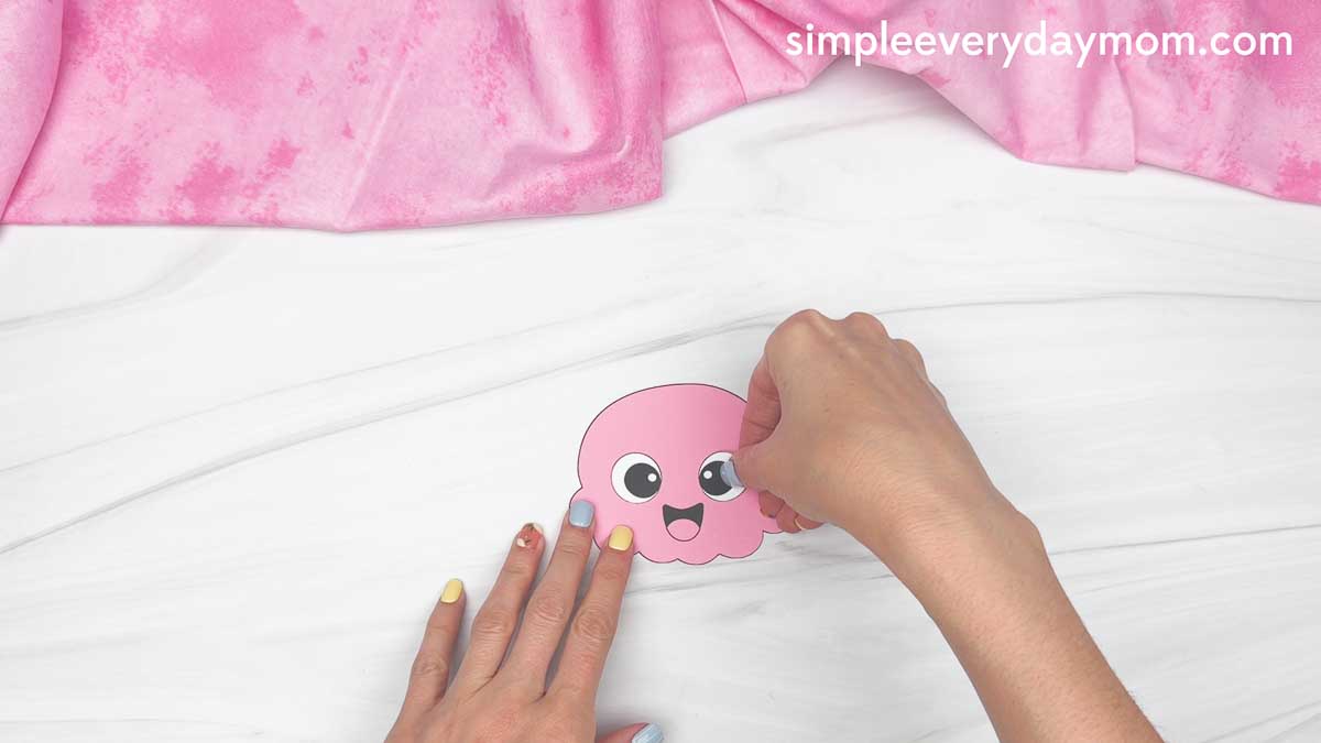 Hands placing an eye sticker on a pink ice cream scoop cutout.
