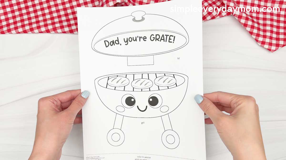 Hands holding a printable Father’s Day grill craft coloring page with a cute smiling grill and the phrase Dad you’re GRATE above it