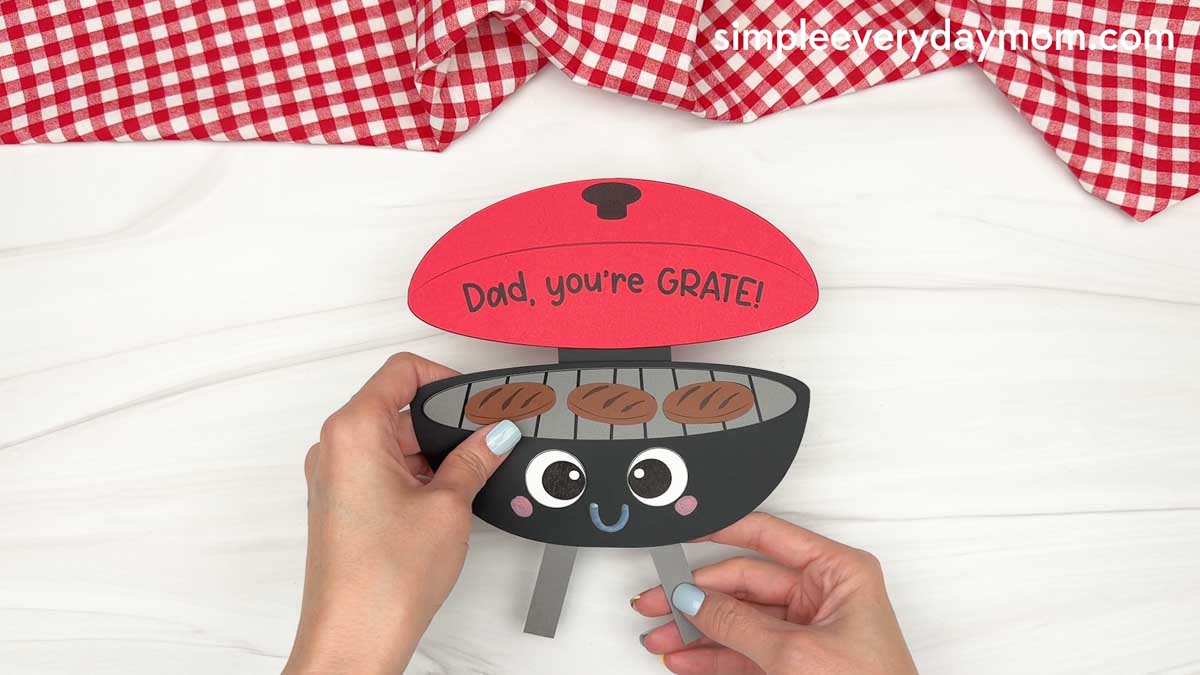 Hands holding the assembled Father’s Day grill craft with smiling face, burger patties, and Dad you’re GRATE message