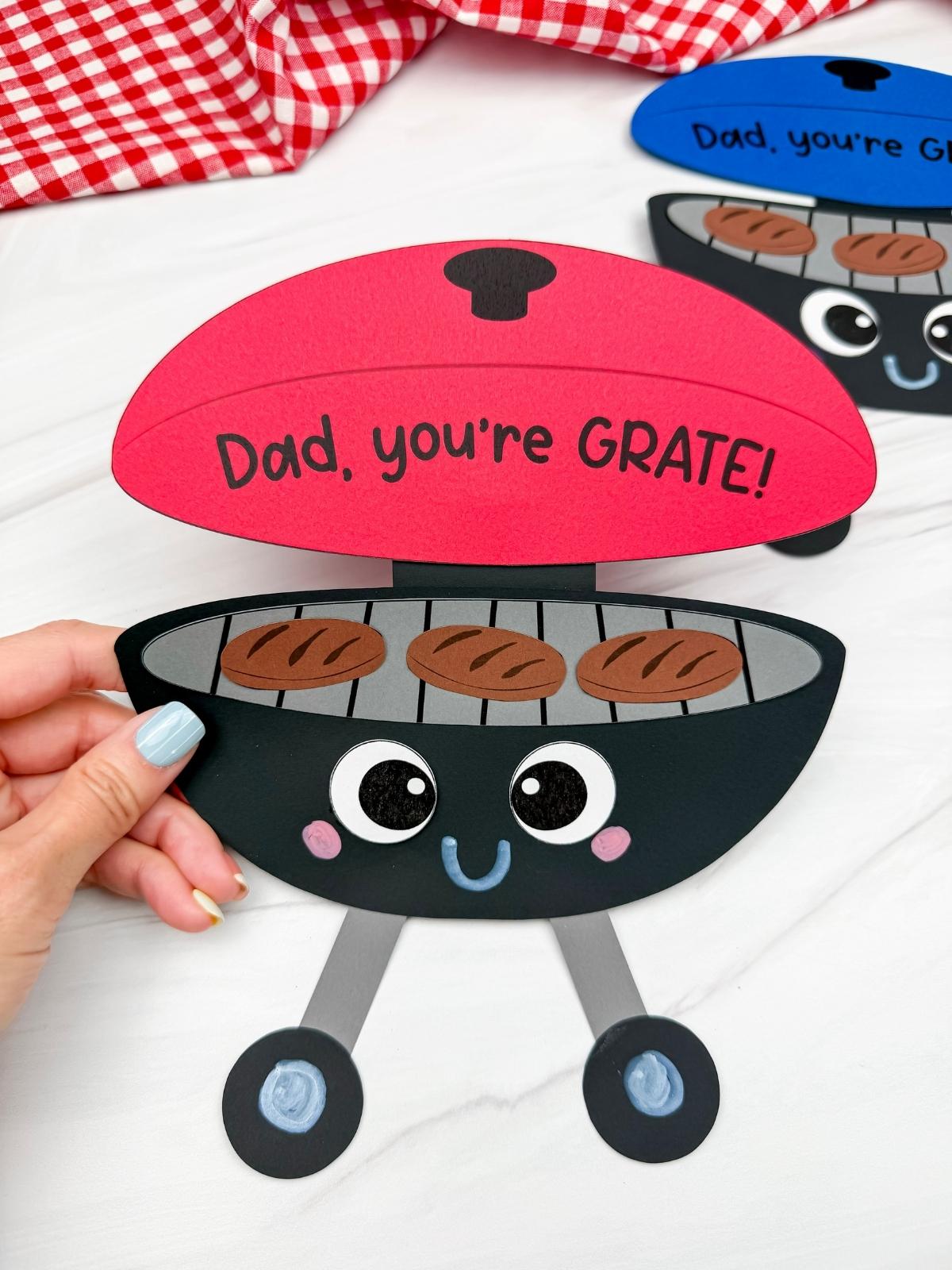 Hands holding a completed Father’s Day grill craft with red lid and Dad you’re GRATE message