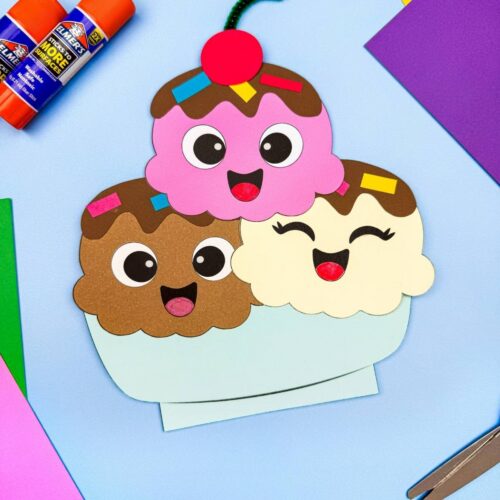 A completed craft of a smiling ice cream sundae with three scoops surrounded by craft supplies