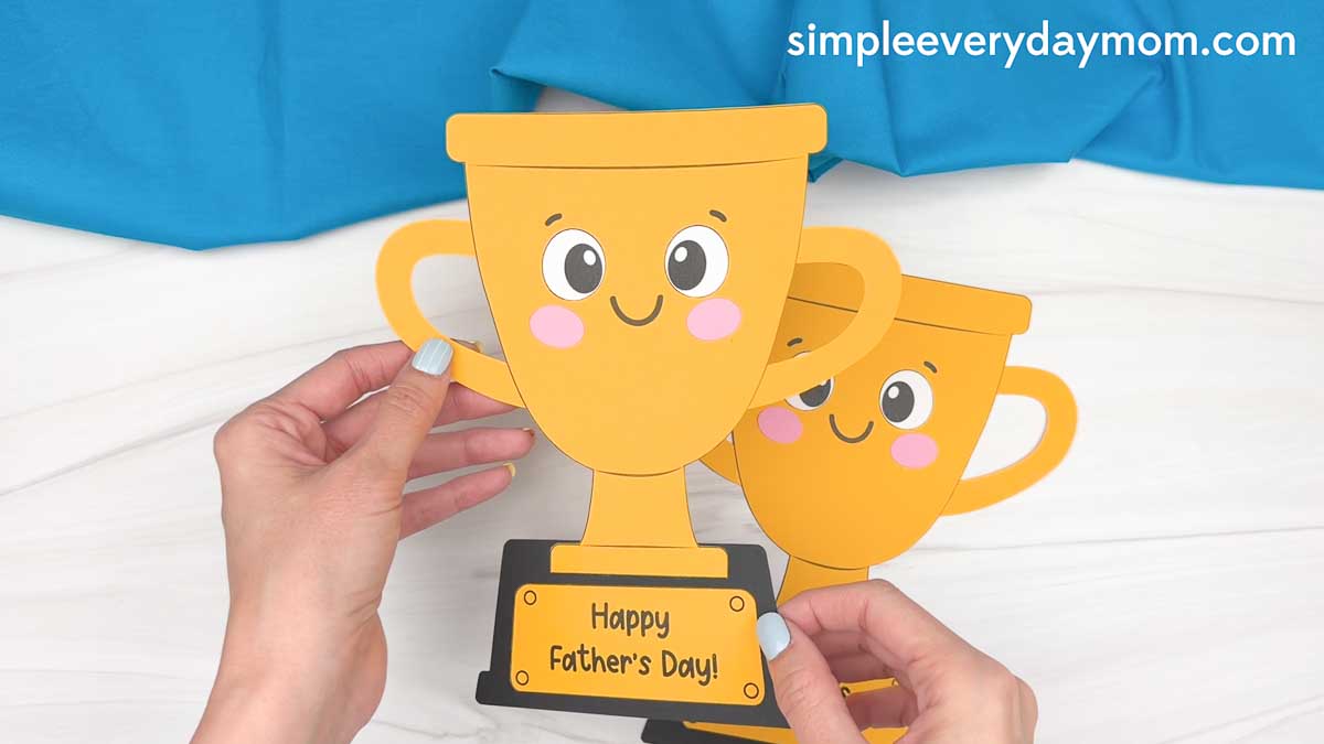 Hands holding completed Father’s Day trophy crafts with smiling faces and a Happy Father’s Day message.
