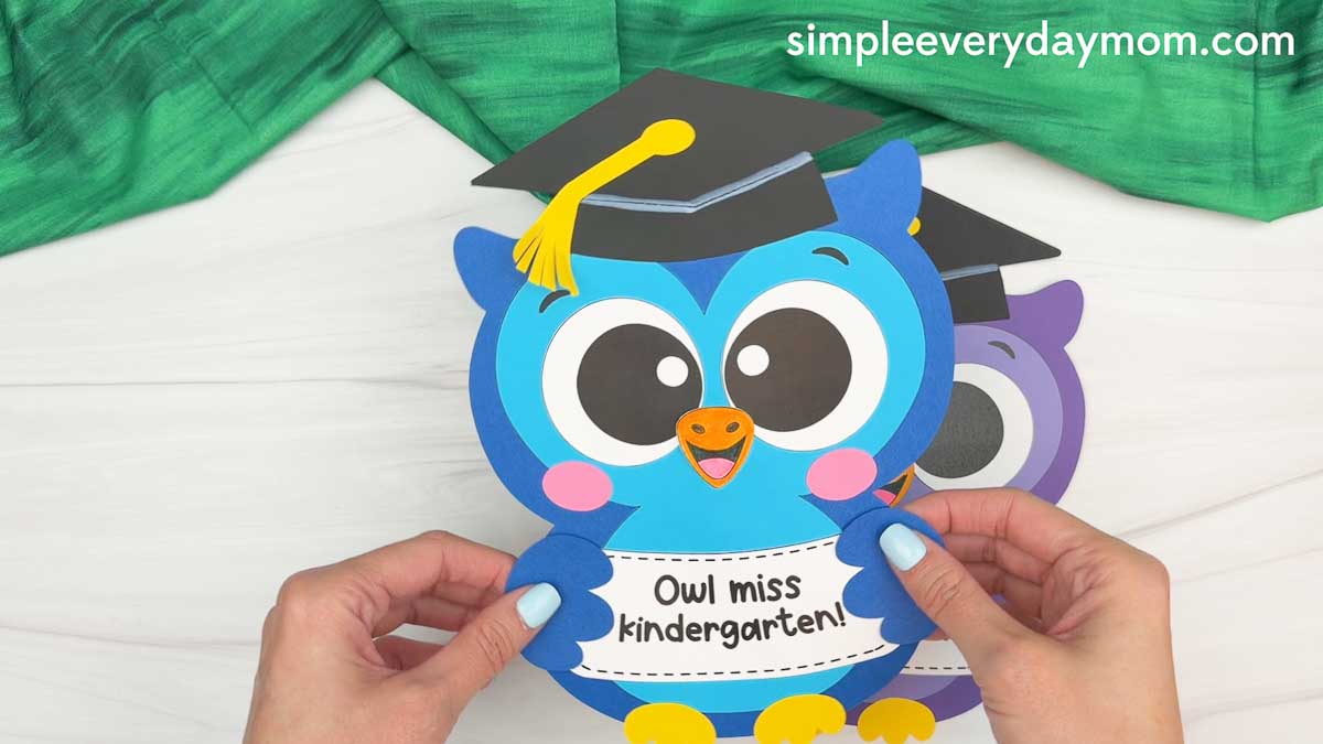 Hands holding a completed owl graduation craft with a graduation cap and “Owl miss kindergarten!” message.