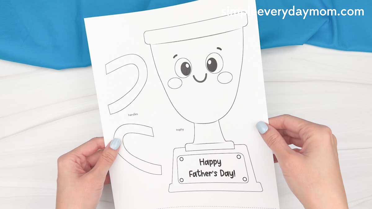 Hands holding a printable Father’s Day trophy craft template with cut out pieces and a Happy Father’s Day message.