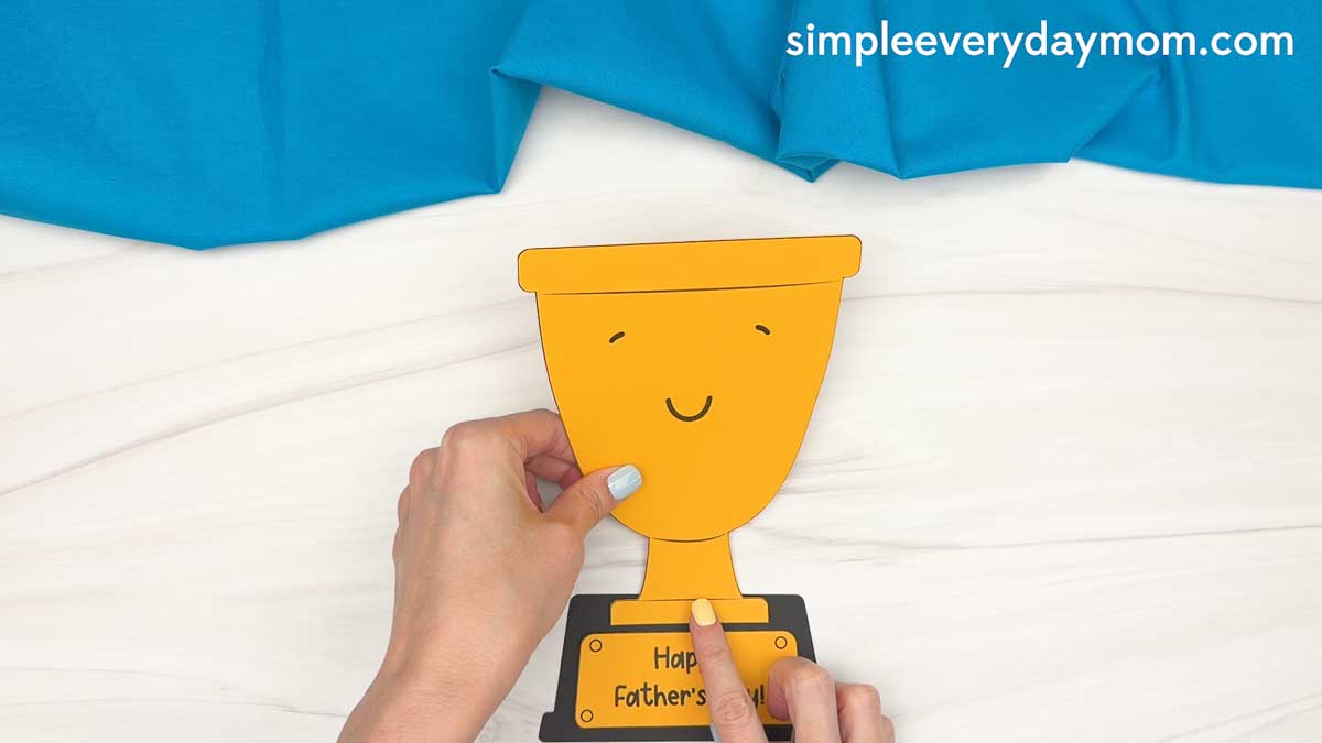 Hands holding the Father’s Day trophy craft while attaching the trophy piece to the base.