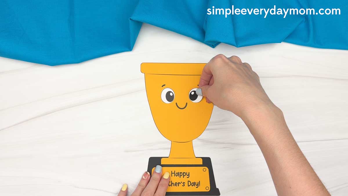 Hands attaching the eye piece to the smiling Father’s Day trophy craft.