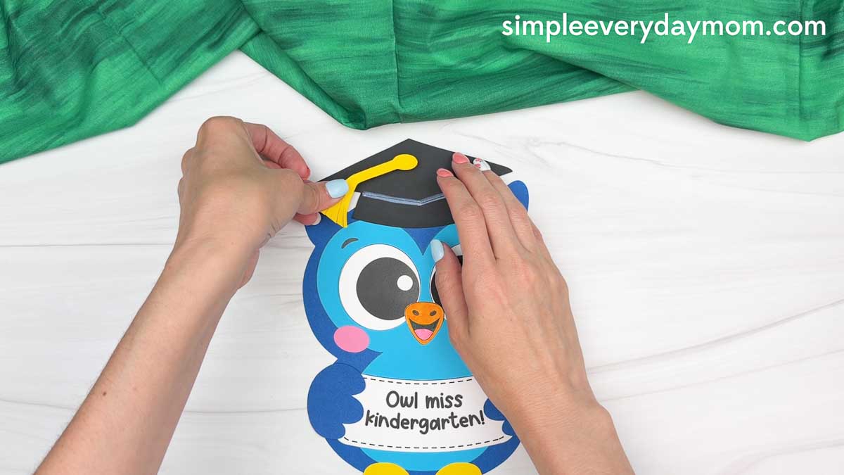 Hands attaching the yellow tassel to the graduation cap on the owl graduation craft.