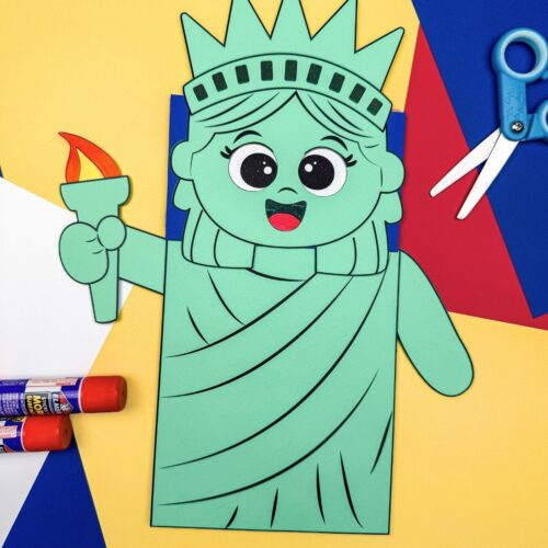 A completed craft showing a Statue of Liberty paper bag puppet with craft supplies on a yellow background.