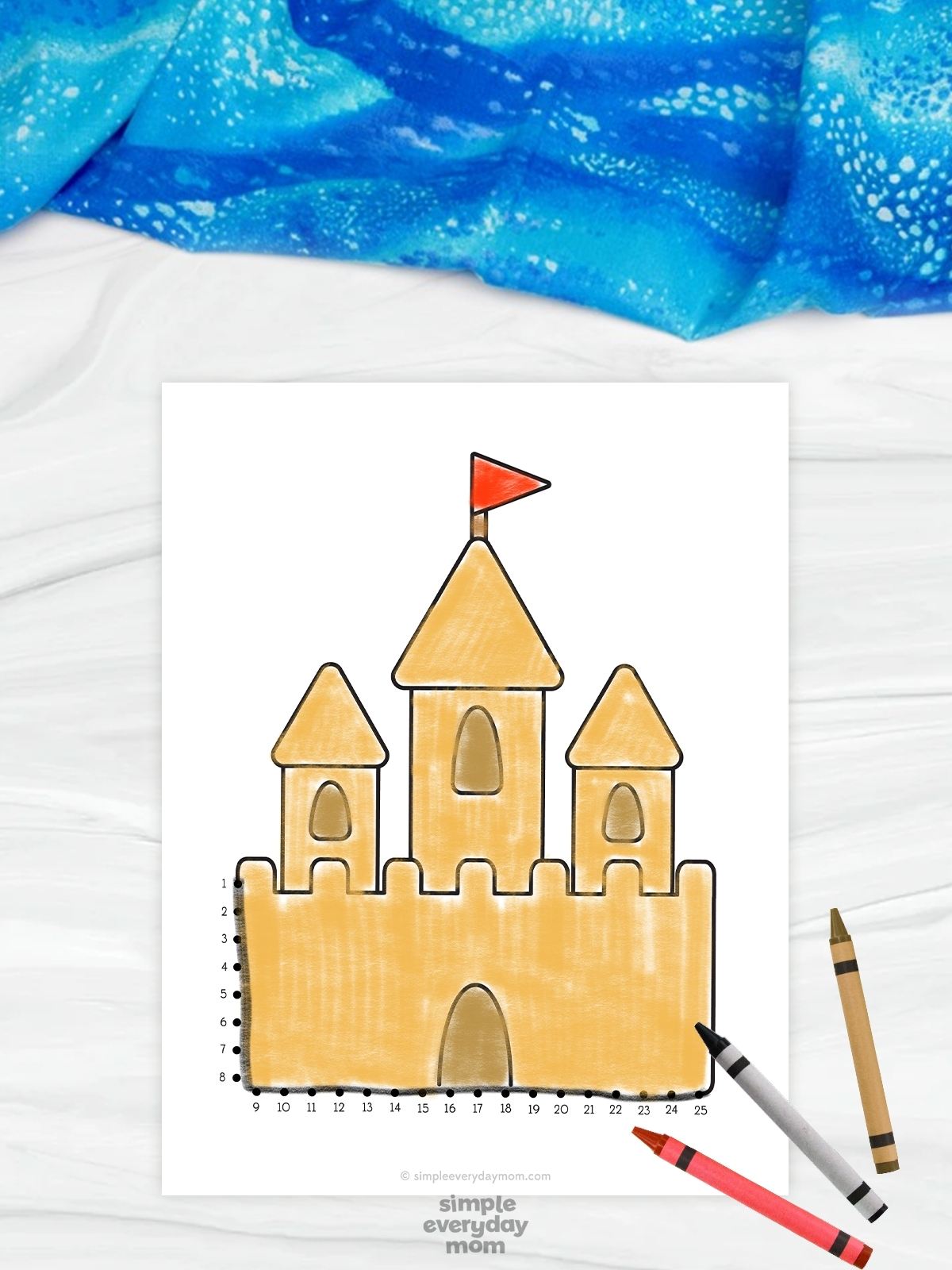 The image features a beach-themed connect-the-dots worksheet showing a large sandcastle with three towers and a red flag on top. Numbered dots outline the bottom and side of the castle, allowing children to connect the dots while practicing counting and pencil skills. The worksheet is displayed on a light background with colorful crayons and a blue fabric accent, creating a fun and creative activity for young learners.
