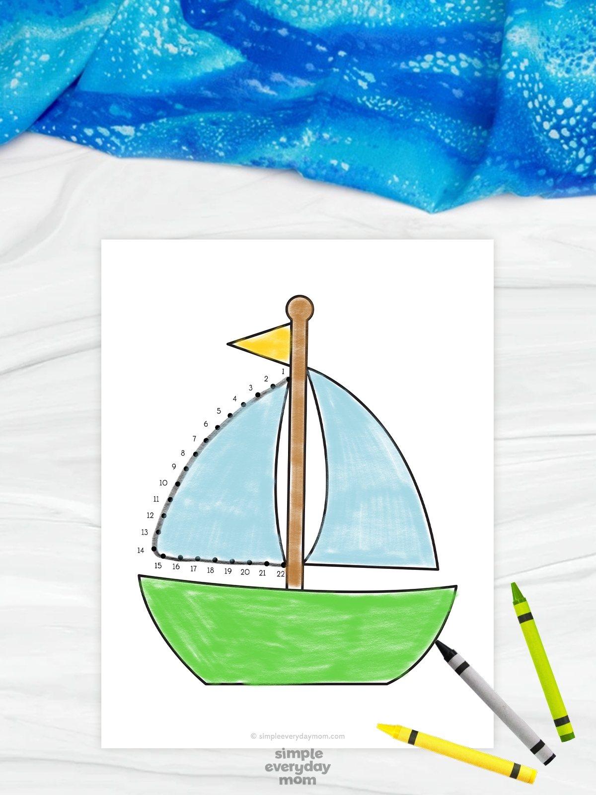 The image features a beach-themed connect-the-dots worksheet with a colorful sailboat illustration. Numbered dots outline one of the blue sails, allowing children to trace and complete the picture while practicing counting and fine motor skills. Bright crayons and a soft blue fabric background create a cheerful and educational activity setting for young learners.