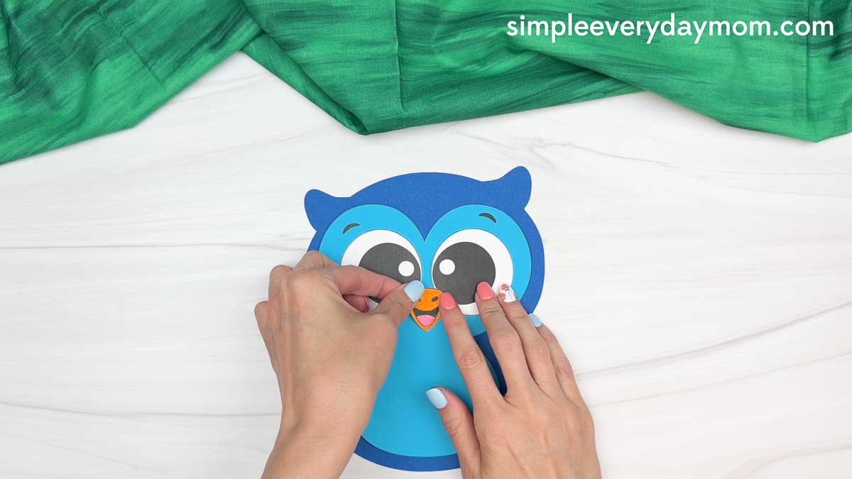 Hands attaching the large owl eyes to the owl graduation craft face.