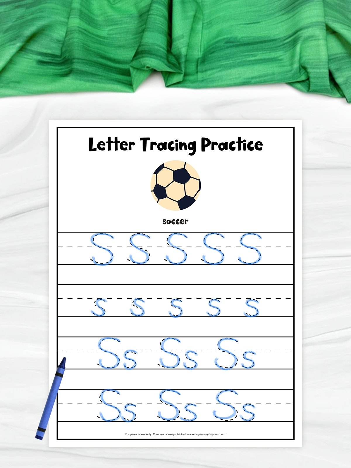 The image shows a children’s worksheet titled “Letter Tracing Practice” focused on the letter “S.” It includes rows of dashed uppercase and lowercase “S” letters for kids to trace, along with a soccer ball illustration as the theme. A blue crayon is placed beside the worksheet, and a green cloth is visible in the background.