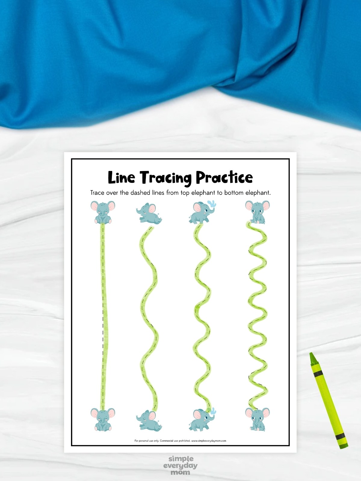 This image features a printable “Line Tracing Practice” worksheet created to help preschool children develop fine motor and handwriting readiness skills. The worksheet includes several wavy green tracing lines that children can follow from the top elephant illustrations to the matching elephants at the bottom. A bright green crayon, cute blue elephant characters, and a soft blue fabric background give the activity a playful and child-friendly appearance.