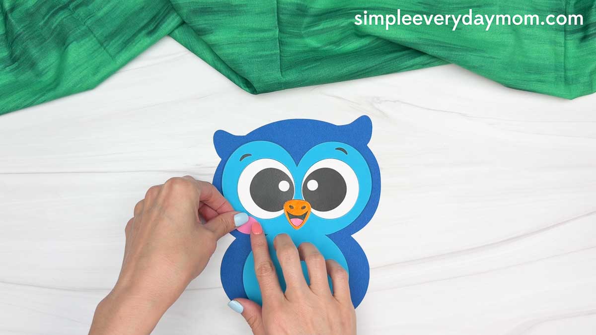 Hands attaching the pink owl cheeks to the owl graduation craft face.