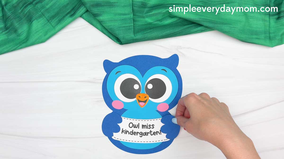 Hands attaching the owl wings to the owl graduation craft sign.