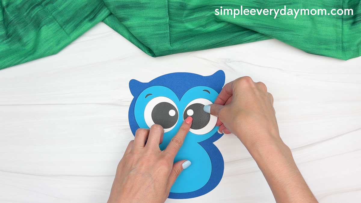 Hands attaching the large owl eyes to the owl graduation craft face.