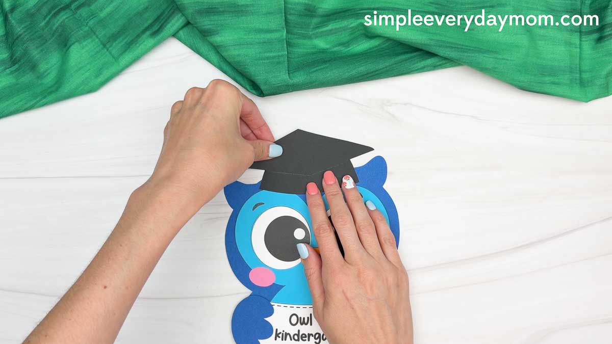 Hands placing the graduation cap onto the owl graduation craft.
