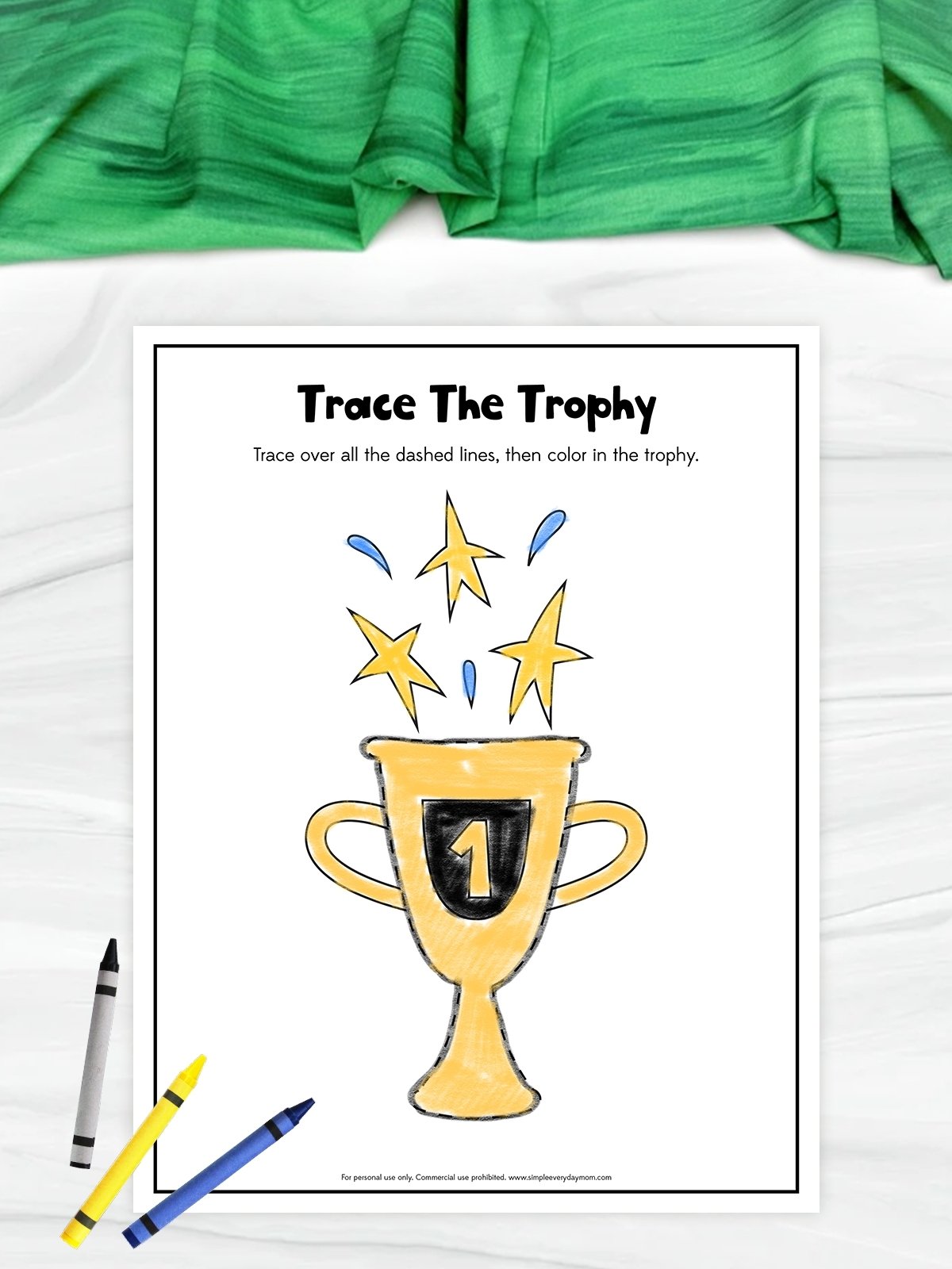 This image shows a printable worksheet titled “Trace The Trophy” designed for children to practice tracing and coloring skills. The worksheet features a large trophy with a number one symbol, along with stars and decorative shapes above it for tracing practice. Crayons placed around the page and the bright yellow trophy give the activity a fun and creative appearance for young learners.