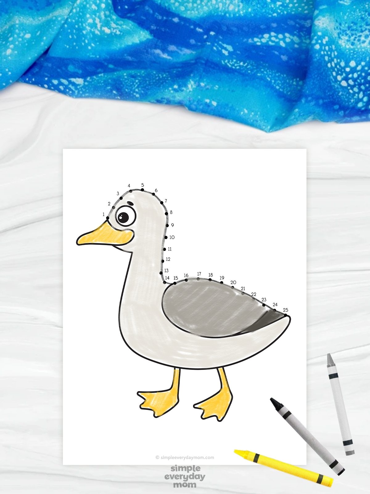 The image shows a beach-themed connect-the-dots worksheet featuring a cute gray duck with a yellow beak and feet. Numbered dots trace along the duck’s head and back, helping children practice counting and fine motor skills while completing the picture. The worksheet is displayed on a light background with crayons and a blue fabric accent, creating a fun and engaging educational activity for kids.