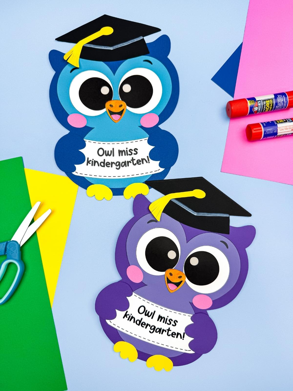 A completed craft featuring blue and purple owl graduation crafts surrounded by colorful paper, scissors, and glue sticks.