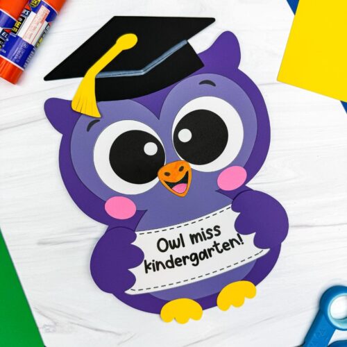 Hands holding a completed purple owl graduation craft with a graduation cap and “Owl miss kindergarten!” sign.